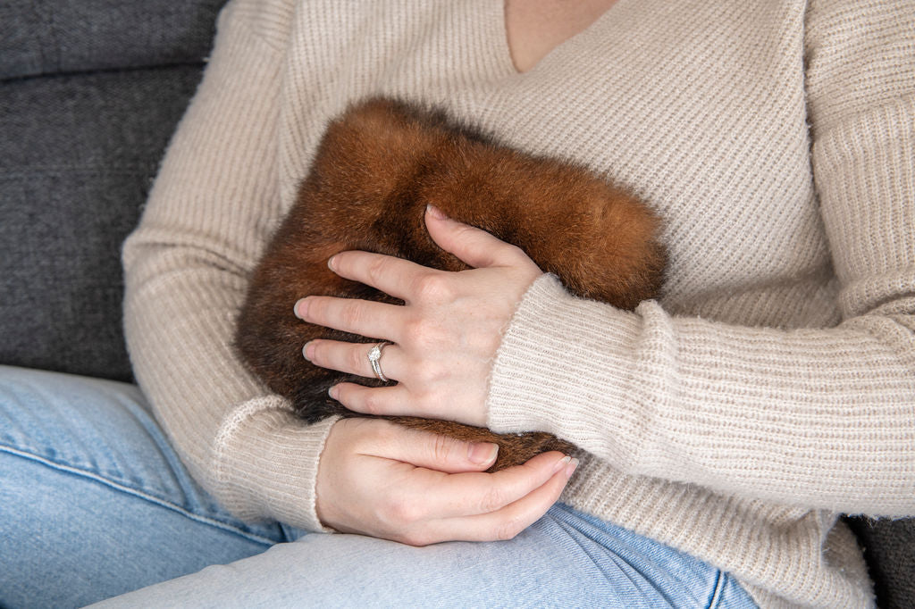 Person holding a brown fur wheat bag cover with a neutral background