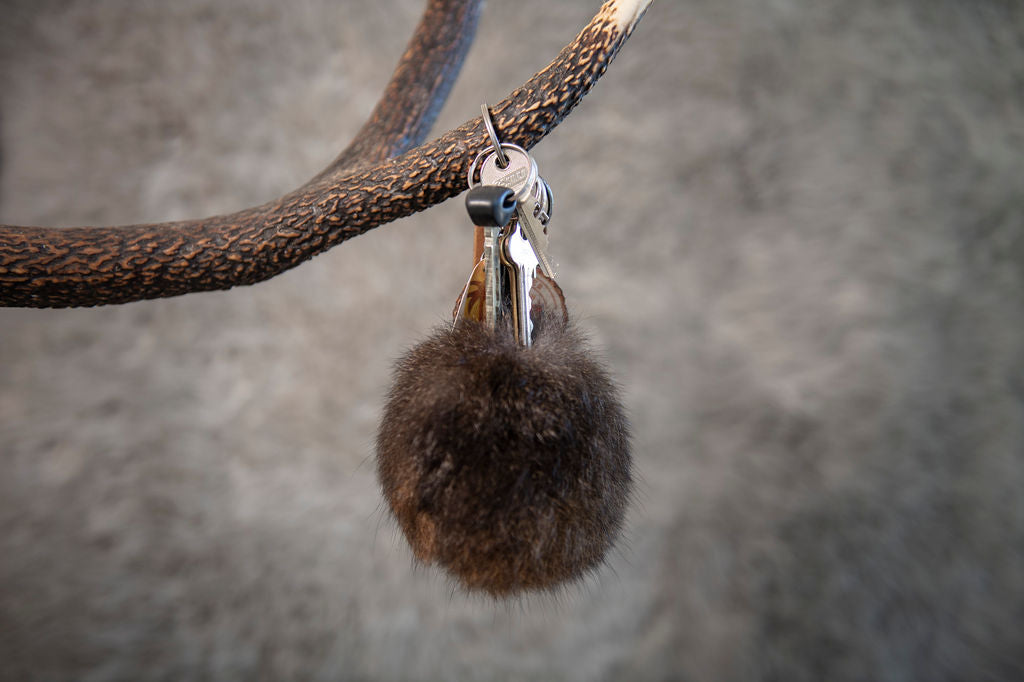 Keychain with a brown fuzzy ball attached to a branch against a blurred background