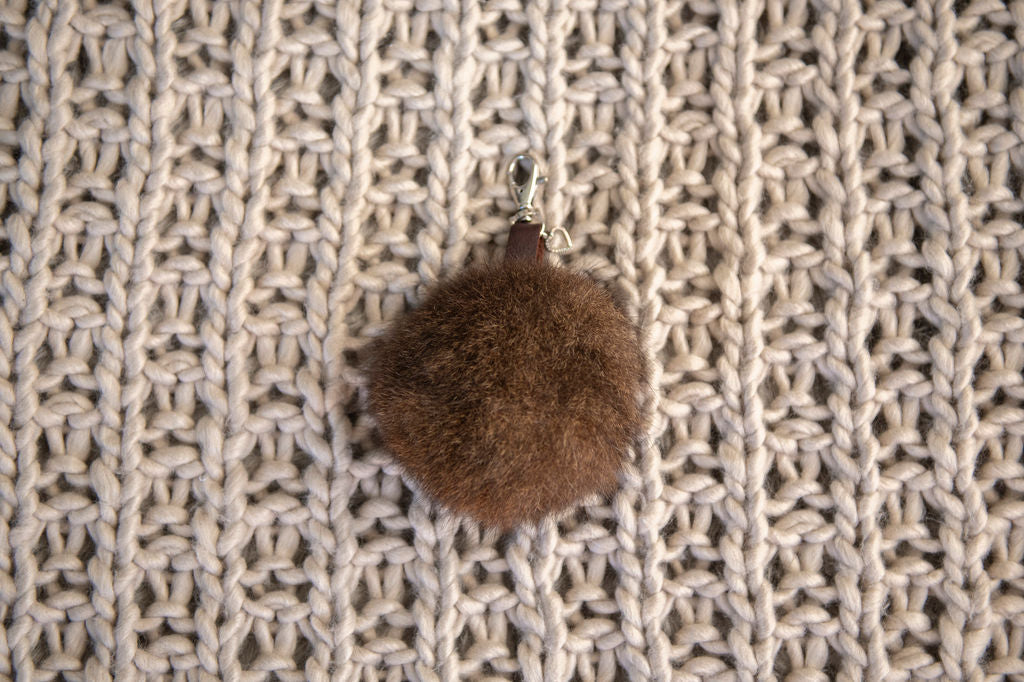 Brown fuzzy keychain on a textured beige fabric background