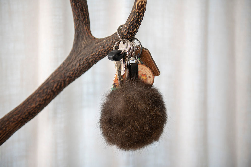 Keychain with a brown fur pom-pom and wooden accents hanging from a branch against a neutral background